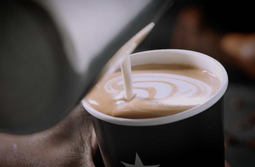 A flat white in a grey cup on a saucer, with a biscuit alongside